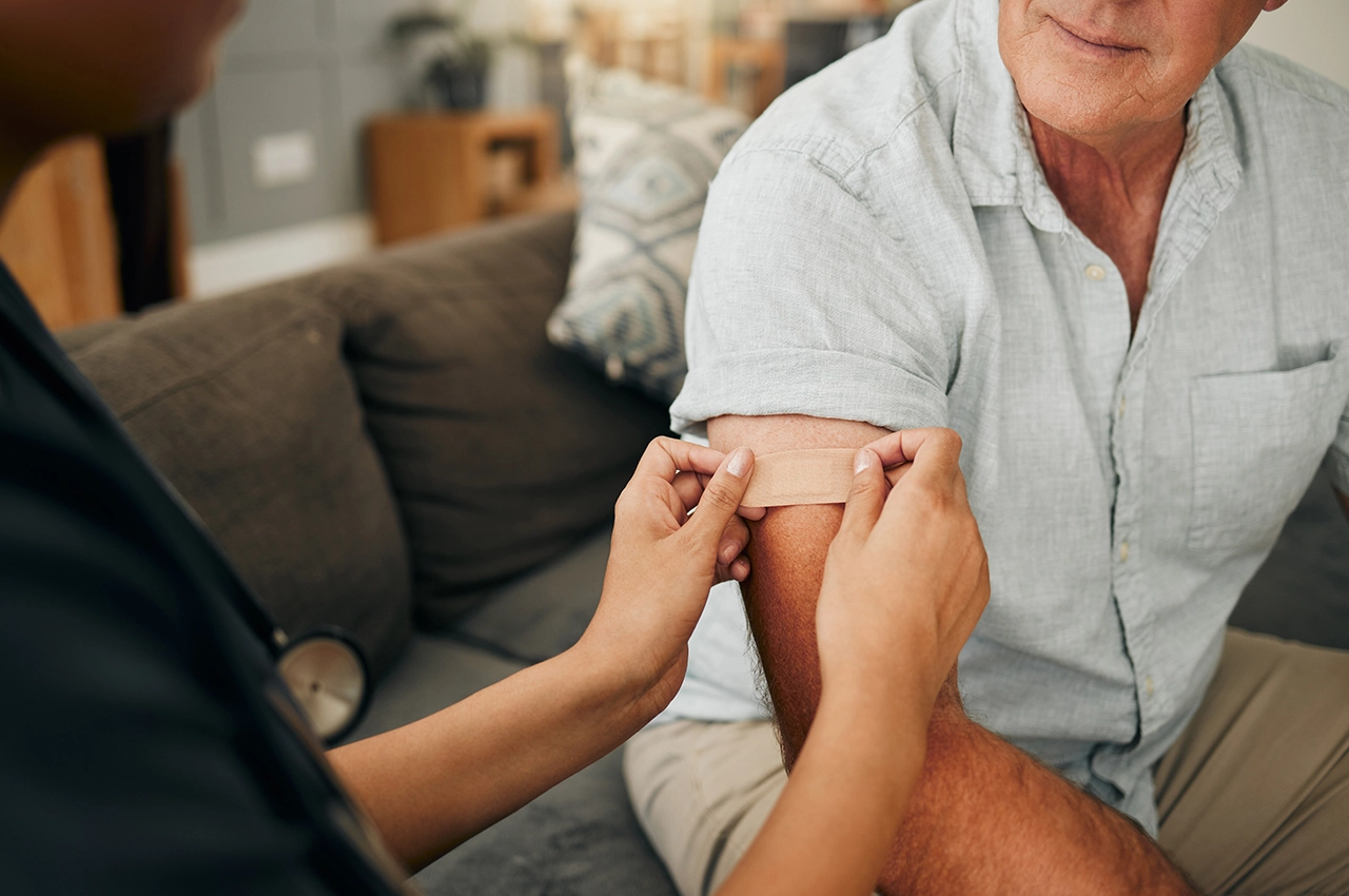 ممرضة تضع لاصقًا طبيًا على ذراع رجل بعد إعطائه حقنة عضلية أو وريدية في منزله في الشارقة