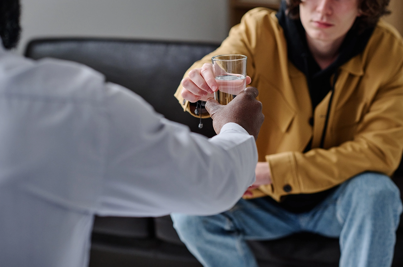 مشهد دعم علاجي بين طبيب ومريض حيث يمرر الطبيب كوب من الماء للمريض خلال جلسة علاج حالات الإدمان في الشارقة